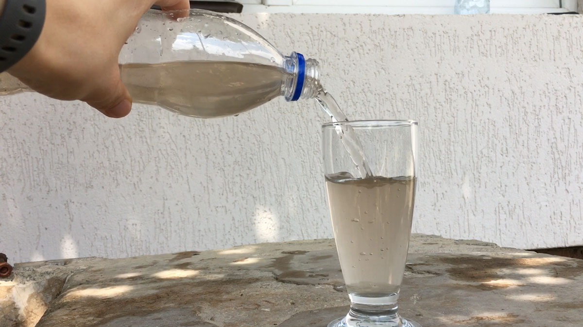 Фотографија на која од шише се истура во чаша нечиста вода.