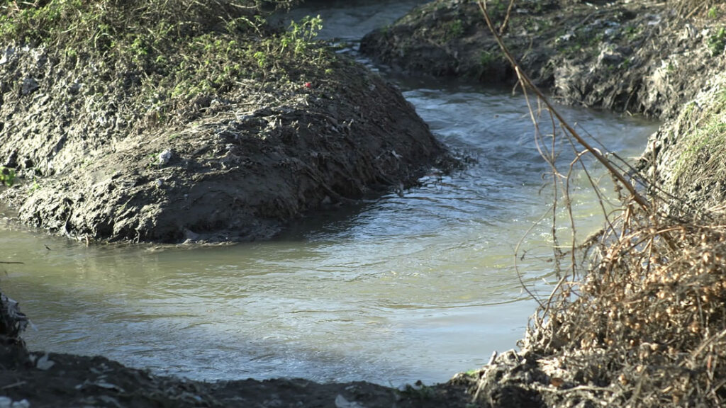 Фотографија на која се гледа мало корито од река опркужено со ѓубре