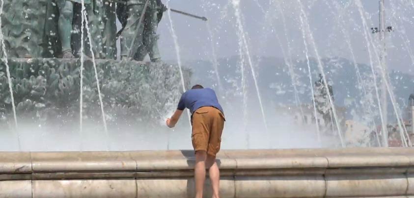 Човек се разладува на фонтана во центарот на Скопје.